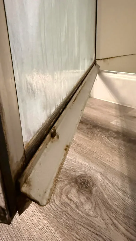 Shower door track with heavy build-up before cleaning by Dolane Cleaning Services